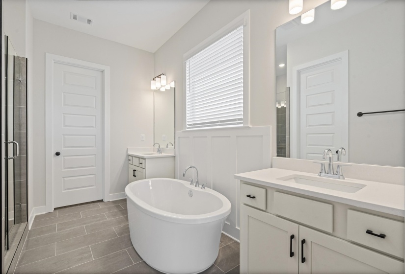 Spacious bathroom featuring a freestanding soaking tub, dual vanities with integrated sinks, and a glass-enclosed shower