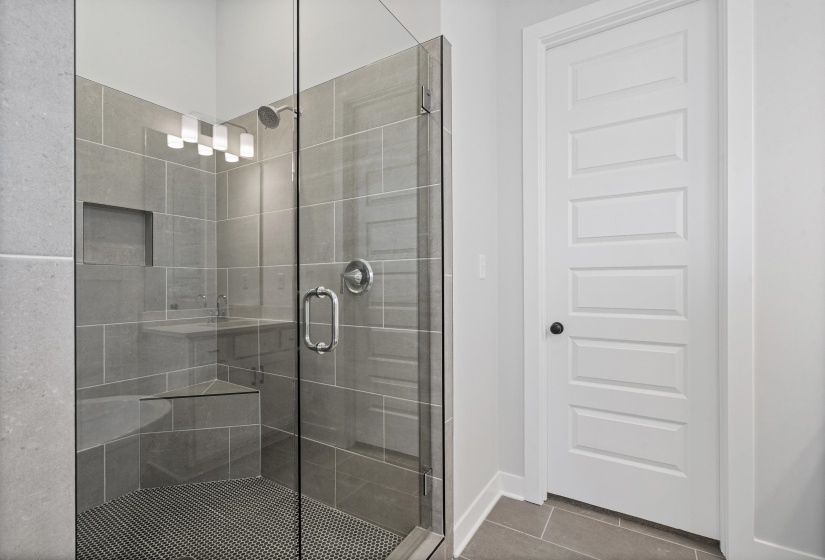 Glass-enclosed shower featuring large format gray wall tiling, a built-in corner bench, a recessed shower niche, and a circular mosaic tile floor