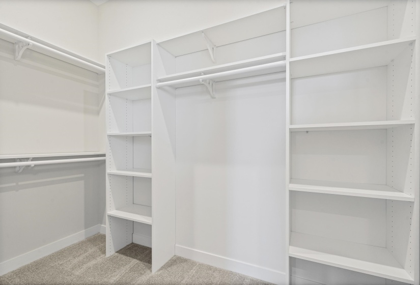 Walk-in closet featuring white built-in shelving, multiple hanging rods, and gray carpet flooring