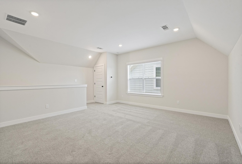 Loft space featuring soft gray carpeting, a single window with blinds, recessed lighting, a built-in railing, and a paneled door