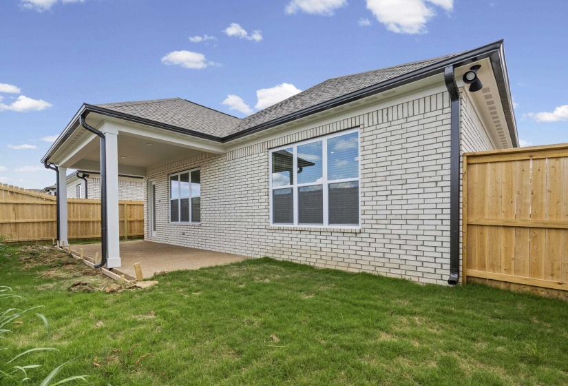 Rear exterior featuring a covered patio with concrete flooring, white brick siding, a dark shingle roof, and black rain gutters