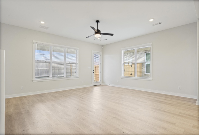 Spacious room featuring light wood-finish flooring, white walls, and multiple windows