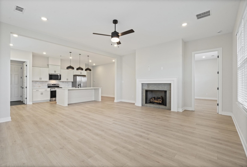 Open-concept living space featuring wood-finish flooring, a contemporary fireplace with a white mantel, and a kitchen island with pendant lighting
