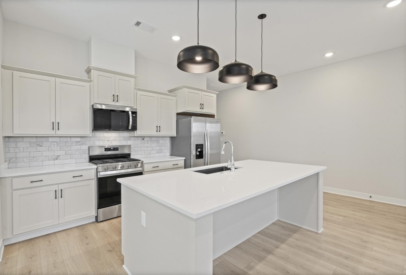 Modern kitchen featuring light-toned cabinetry with dark hardware, stainless steel appliances, a subway tile backsplash, a large center island with an undermount sink, and wood-finish flooring