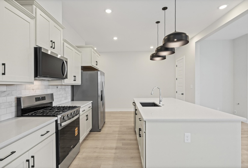 Modern kitchen featuring light-toned cabinetry with black hardware, stainless steel appliances, a white subway tile backsplash, and light wood-finish flooring