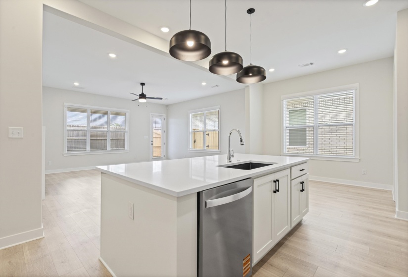 Kitchen island featuring a white countertop, stainless steel sink, pull-down faucet, and integrated dishwasher