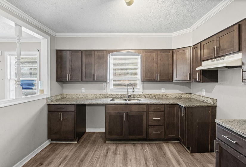 Kitchen with dark brown cabinets, a textured ceiling, ornamental molding, under cabinet range hood, and dark wood-style flooring