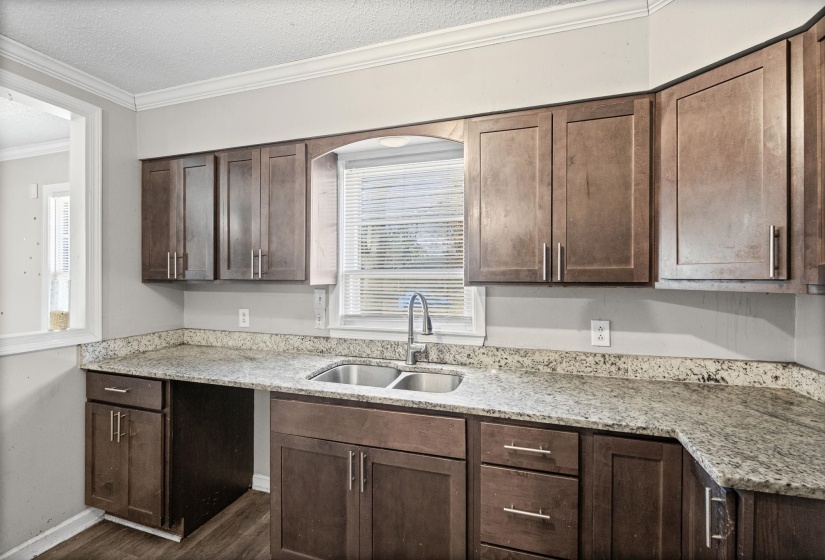Kitchen featuring dark brown cabinets, light stone countertops, ornamental molding, a textured ceiling, and dark wood-type flooring