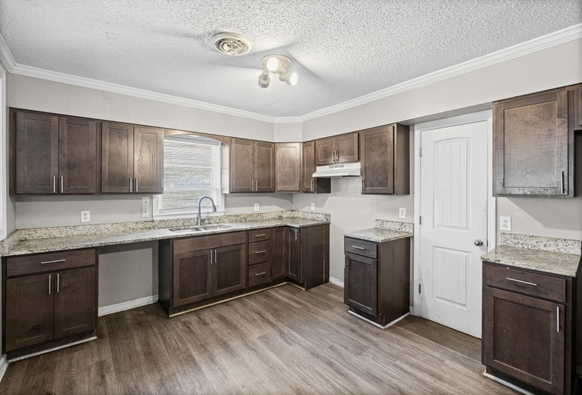 Kitchen with dark brown cabinets, a textured ceiling, ornamental molding, light stone counters, and dark wood finished floors