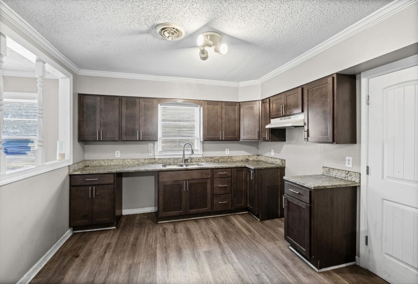Kitchen featuring dark brown cabinetry, a textured ceiling, ornamental molding, dark wood-style flooring, and light stone countertops