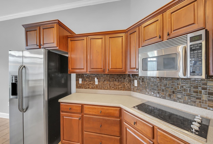 Kitchen featuring wood cabinetry, stainless steel appliances, a built-in microwave, a glass cooktop, and a tile backsplash