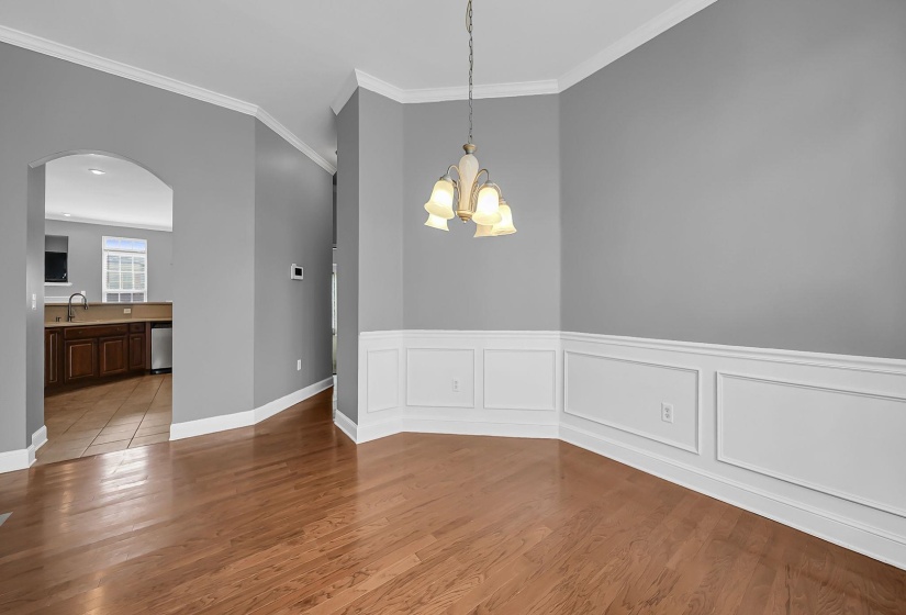 Interior room featuring hardwood flooring, wainscoting, crown molding, and a decorative chandelier