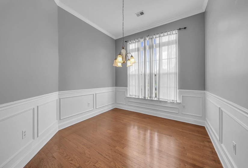 Room featuring wood-finish flooring, two-tone painted walls with wainscoting, crown molding, a window with trim, and a ceiling-mounted light fixture