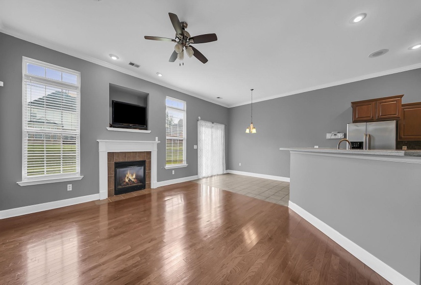 Open-concept living space with rich wood-finish flooring, a contemporary fireplace with a tile surround, and a ceiling fan