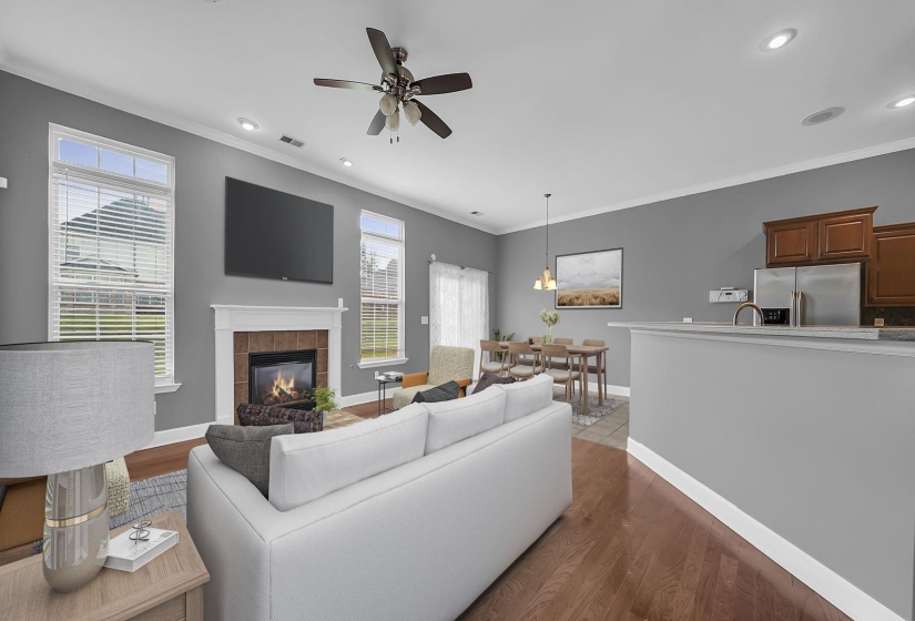 Open-concept living area with wood-finish flooring, a fireplace featuring a brick surround and white mantel, and recessed lighting