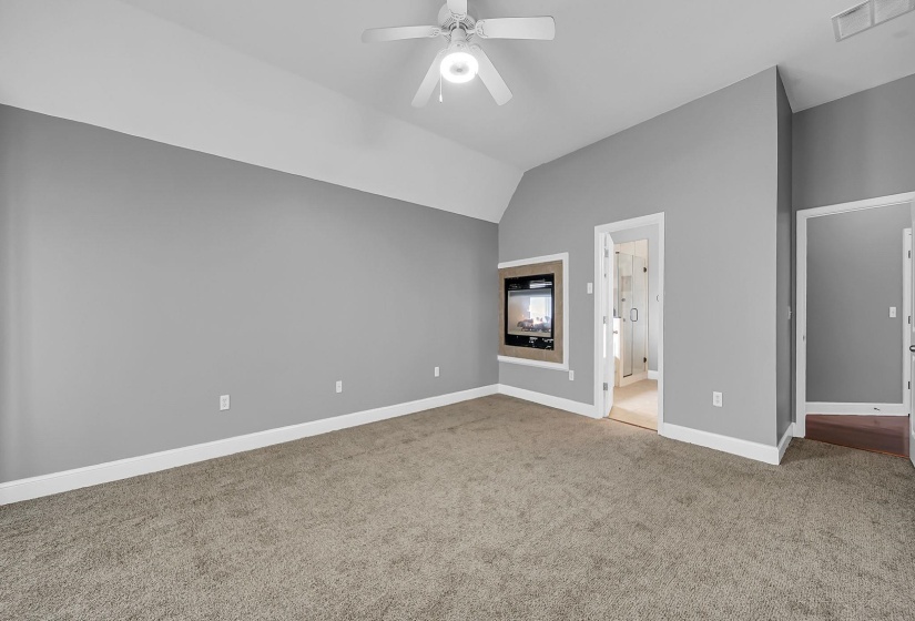 Spacious room featuring vaulted ceilings, a ceiling fan, plush carpet flooring, and a built-in electric fireplace with a wood-finish surround
