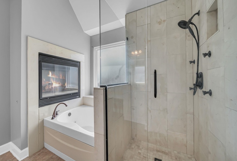 Soaking tub with bronze-finish faucet, built-in fireplace, and adjacent glass-enclosed shower with matte black fixtures