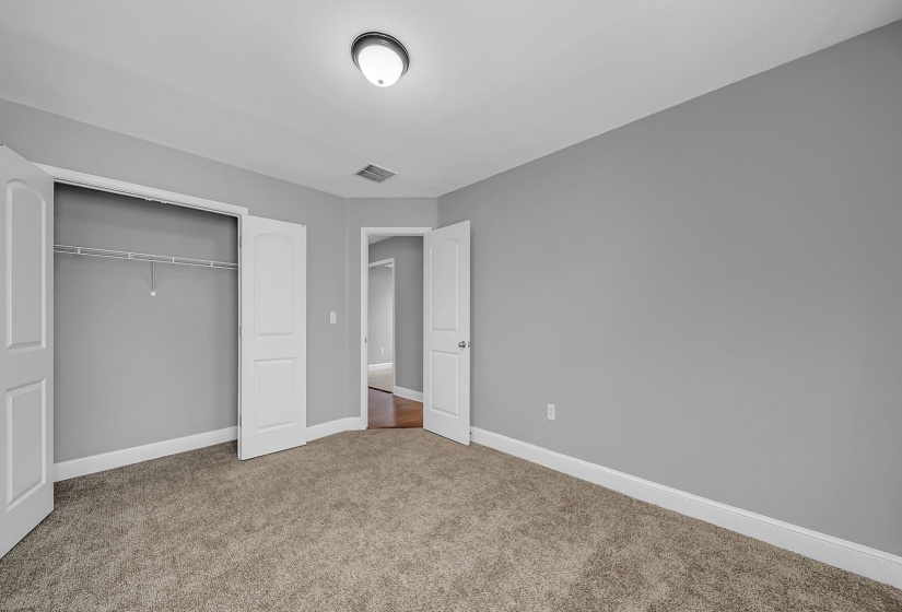 Spacious room featuring neutral carpeting, light gray walls, white trim, a built-in closet with wire shelving, and an overhead flush-mount light fixture