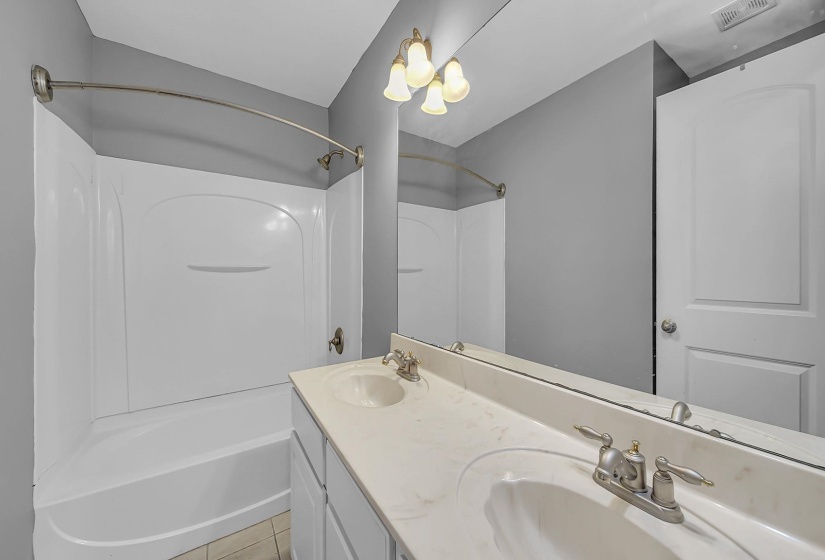 Bathroom featuring a dual vanity with integrated sinks, a full-width mirror, and a shower-tub combination with a curved shower rod