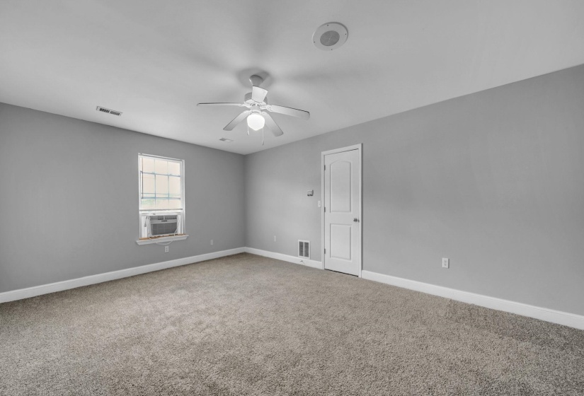 Spacious room featuring neutral gray walls, light-colored carpeting, a ceiling fan with light fixture, and a white interior door