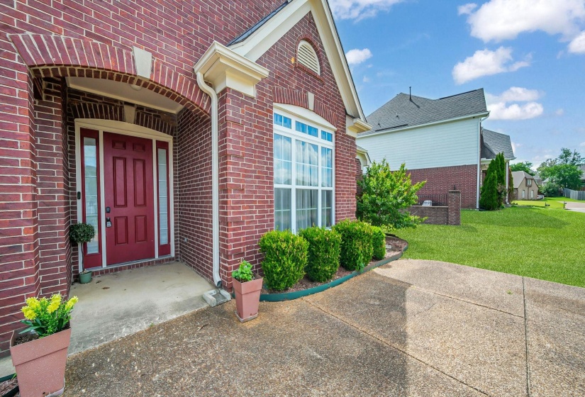 Brick exterior featuring a covered entry, classic red door with sidelights, and a prominent front window