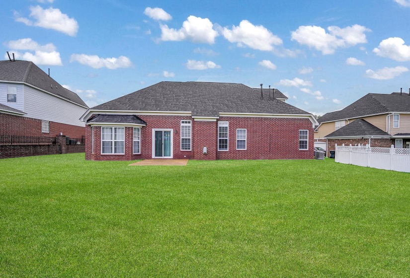 Expansive lawn featuring a red brick exterior, bay window, sliding glass door, and a paver patio