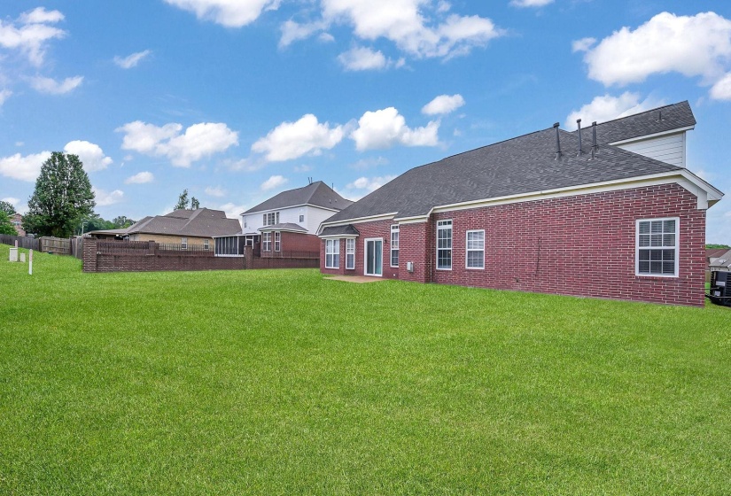 Expansive grassy lawn surrounds a brick exterior home with multiple windows and a sliding glass door