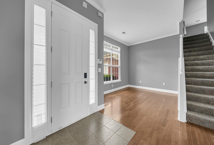 Foyer entrance featuring a white panel door with sidelights, tile flooring, and wood-finish flooring extending into a spacious room with a window