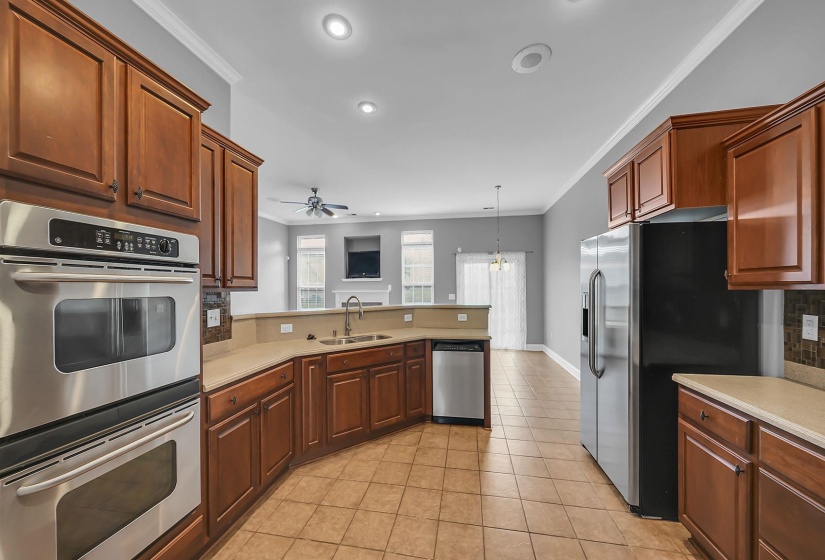Well-appointed kitchen featuring light-toned tile flooring, rich wood cabinetry, stainless steel appliances, and a built-in double oven