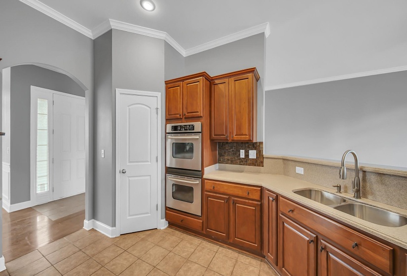 Kitchen featuring wood cabinetry, integrated double ovens, a double basin sink with a high-arc faucet, and tiled flooring