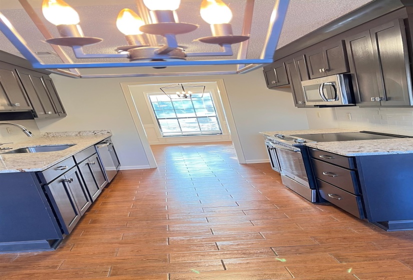 Kitchen featuring light stone counters, stainless steel appliances, backsplash, and light wood finished floors