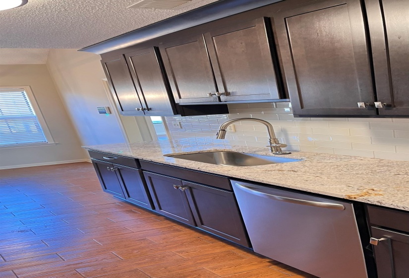 Kitchen with stainless steel dishwasher, light stone counters, tasteful backsplash, light wood finished floors, and a textured ceiling