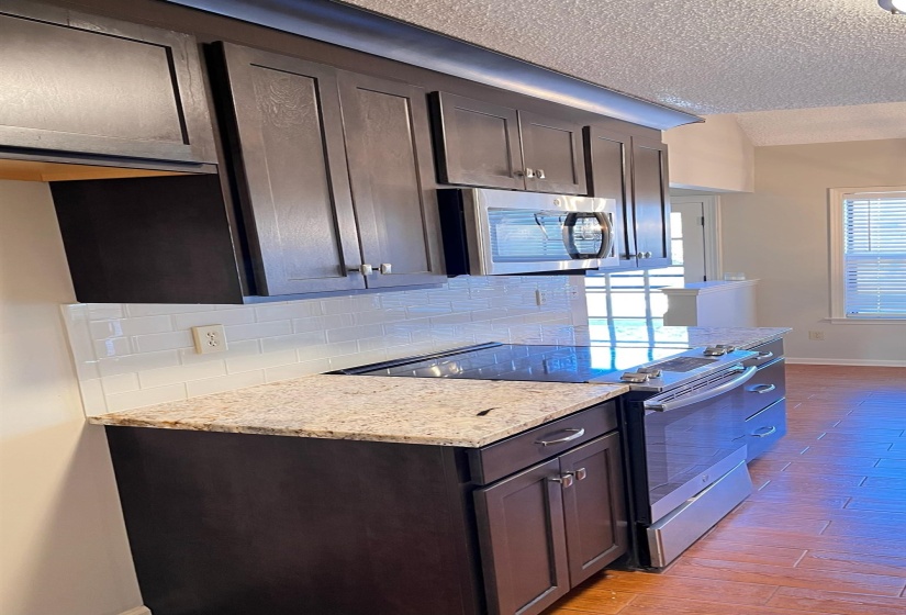 Kitchen with stainless steel appliances, light stone counters, decorative backsplash, dark brown cabinets, and a textured ceiling