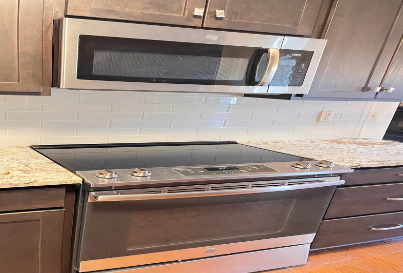 Kitchen featuring stainless steel appliances, dark brown cabinetry, light stone counters, decorative backsplash, and light wood finished floors