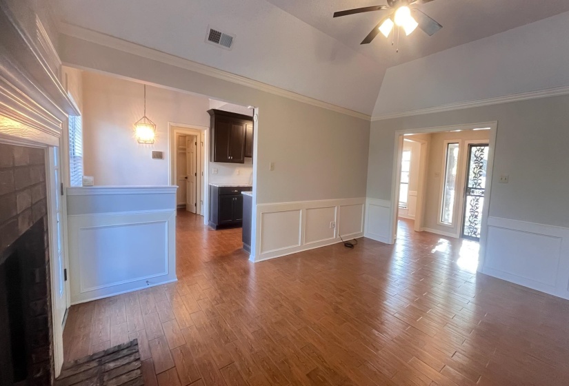 Unfurnished living room with a wainscoted wall, a decorative wall, light wood-style floors, a ceiling fan, and vaulted ceiling