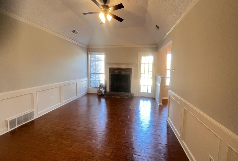 Unfurnished living room with a decorative wall, wainscoting, ornamental molding, dark wood-type flooring, and a brick fireplace