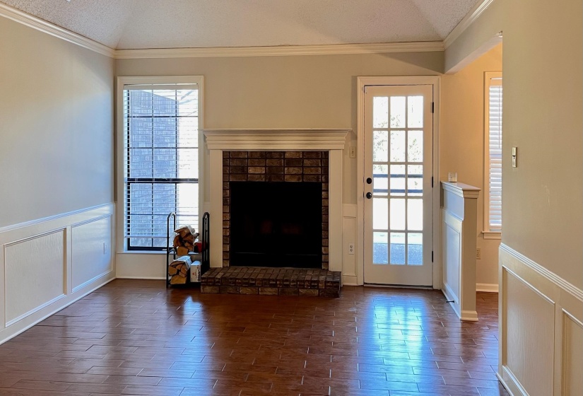 Unfurnished living room with a decorative wall, a fireplace, wood tiled floors, wainscoting, and crown molding