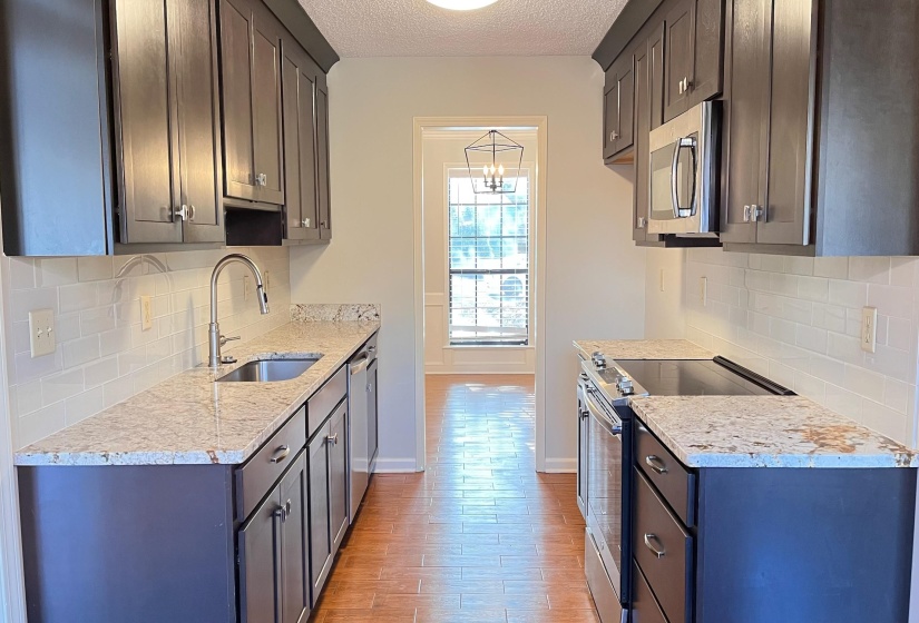 Kitchen with stainless steel appliances, light stone countertops, backsplash, light wood-style floors, and a textured ceiling