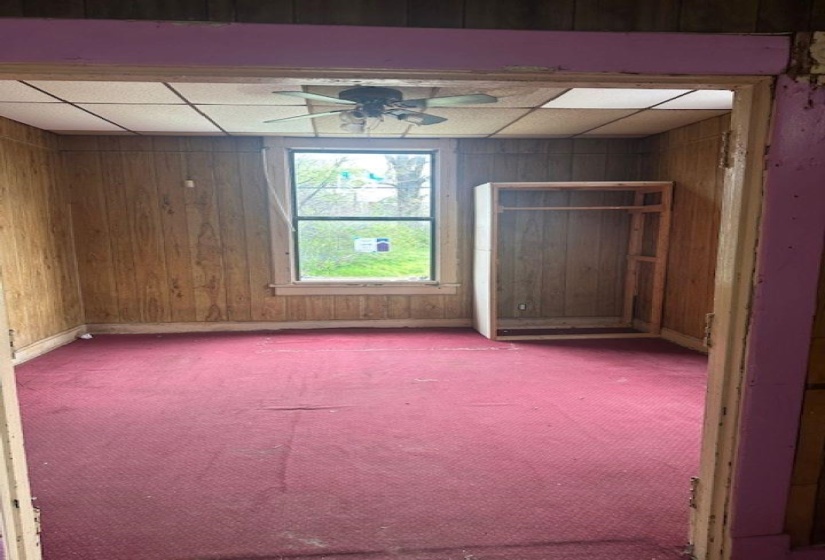 Room featuring wall paneling, a ceiling fan, a window, and a built-in shelving unit
