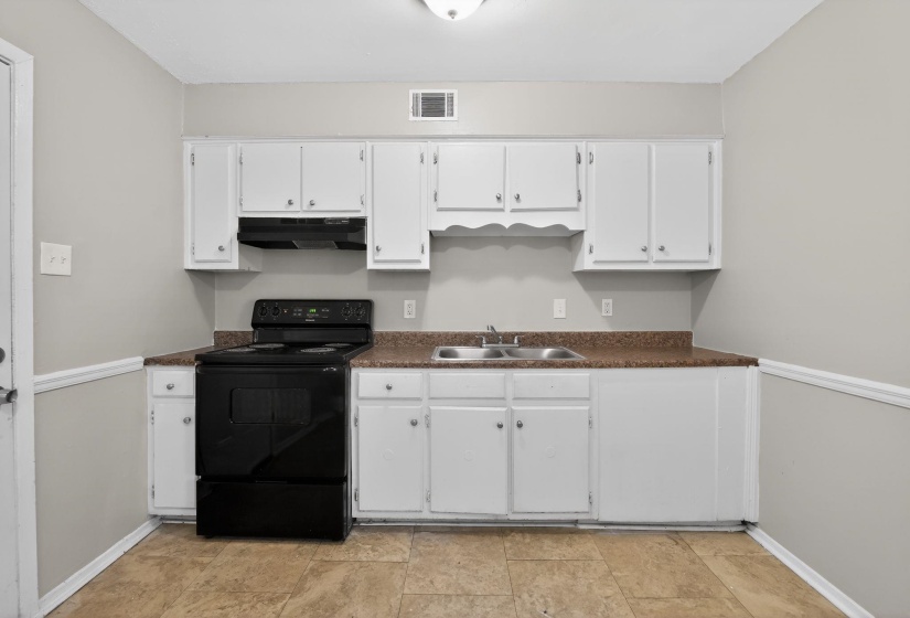 Kitchen featuring black range with electric cooktop, dark countertops, and white cabinetry