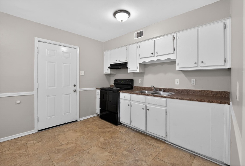 Kitchen with black electric range, dark countertops, white cabinetry, and stone finish flooring