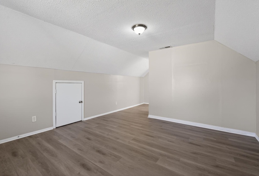 Additional living space with vaulted ceiling, dark wood finished floors, and a textured ceiling