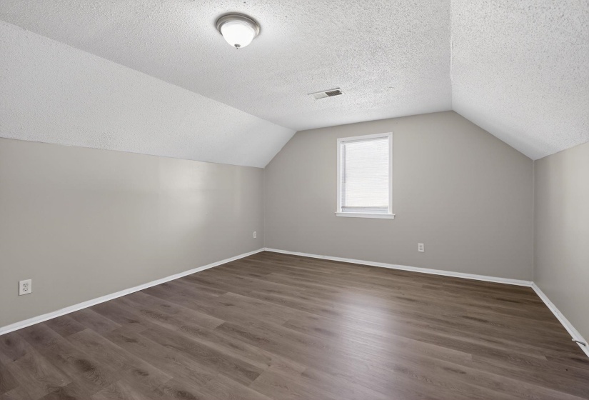 Additional living space featuring lofted ceiling, dark wood-type flooring, and a textured ceiling