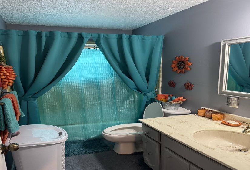 Full bath featuring vanity, shower / bath combo, and a textured ceiling