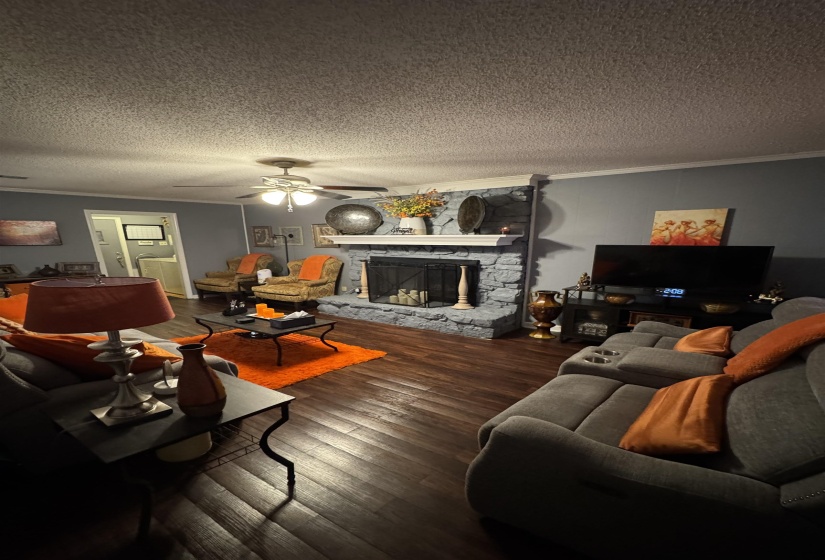Living room with ornamental molding, a stone fireplace, dark wood-style flooring, a ceiling fan, and a textured ceiling