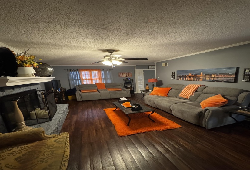 Living room with ornamental molding, a stone fireplace, dark wood finished floors, a textured ceiling, and a ceiling fan