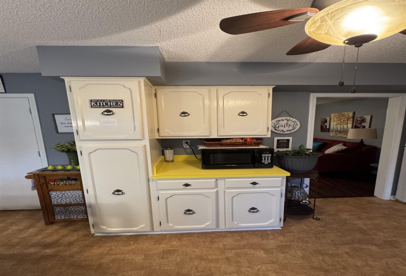 Kitchen with carpet, black microwave, light countertops, a textured ceiling, and ceiling fan