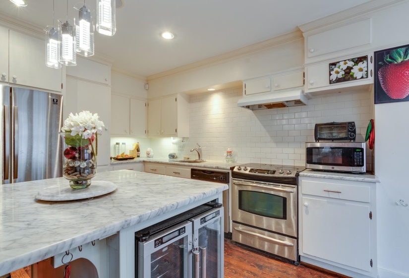Kitchen with stainless steel appliances, white cabinets, crown molding, dark wood-style floors, and beverage cooler