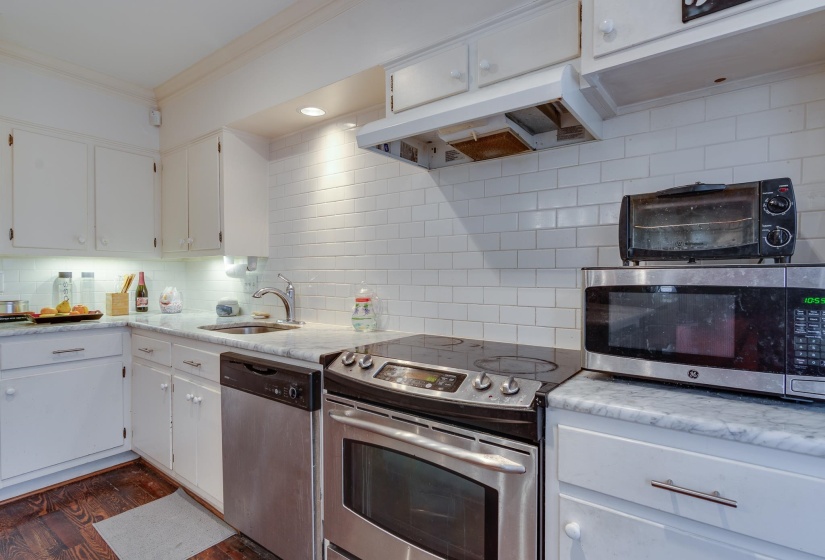 Kitchen featuring appliances with stainless steel finishes, white cabinetry, under cabinet range hood, light stone countertops, and crown molding
