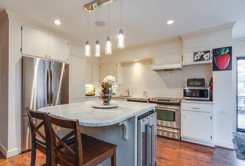 Kitchen featuring decorative light fixtures, appliances with stainless steel finishes, a center island, a breakfast bar, and beverage cooler